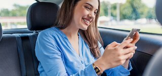 Lächelnde Kundin schaut zufrieden auf ihr Smartphone im Auto — Autohaus Hanstedt @  @ Autohaus Hanstedt