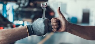 Hand mit Schraubenschlüssel und Daumen nach oben in der Kfz-Werkstatt @ 